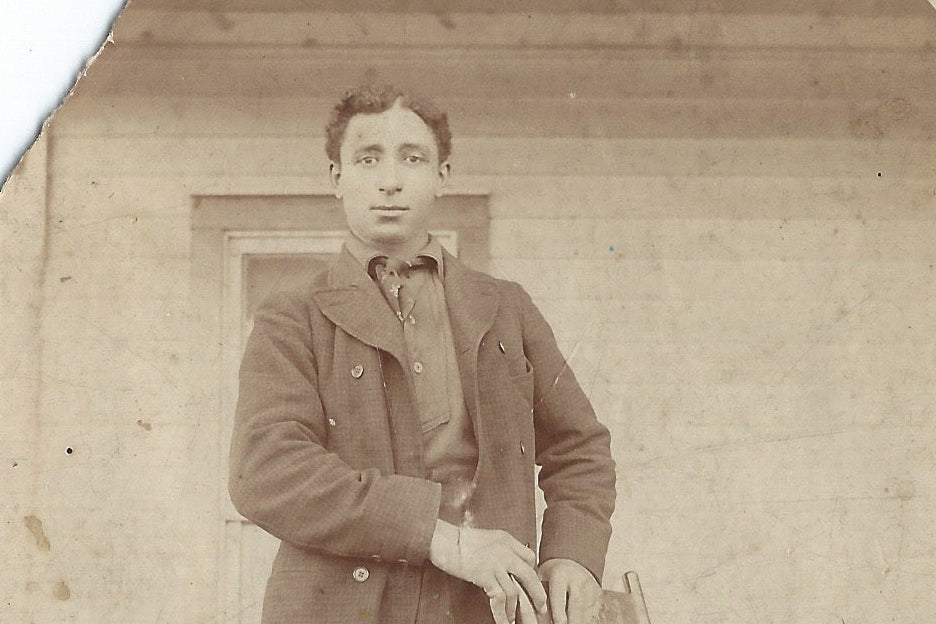 historic photo of man staning with arms on top of chair
